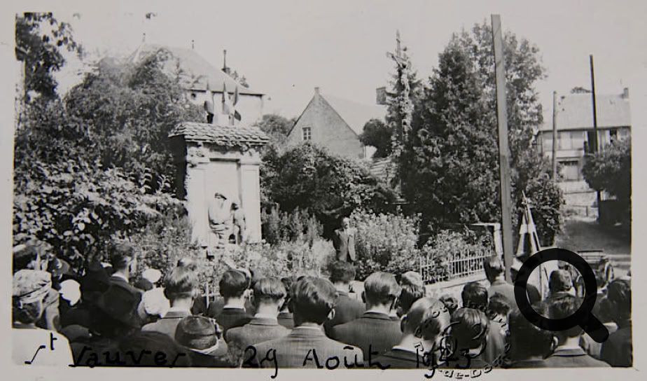 Une foule rassemblée devant un monument entouré de végétation, avec des bâtiments et des arbres en arrière-plan.
