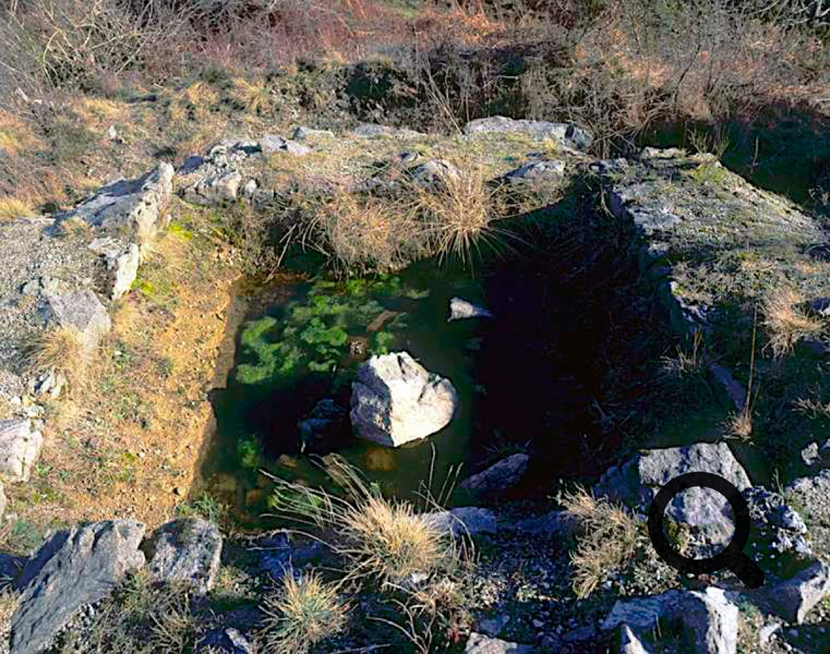 Petite mare entourée de rochers et de végétation sèche.