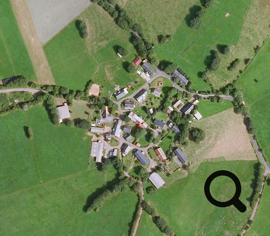 Vue aérienne d'un petit village entouré de champs verts et de routes sinueuses.